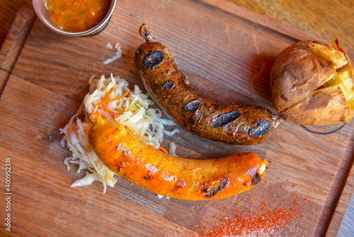BBQ fiery sausages, grilled sausage with potato served on a wooden board with sauce. Eating out in restaurant concept.