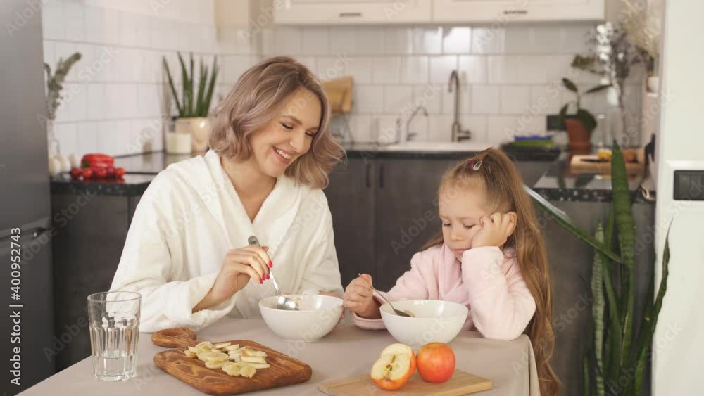 young happy family mother and little daughter sitting at the kitchen table, smiling, enjoying Breakfast or lunch together.