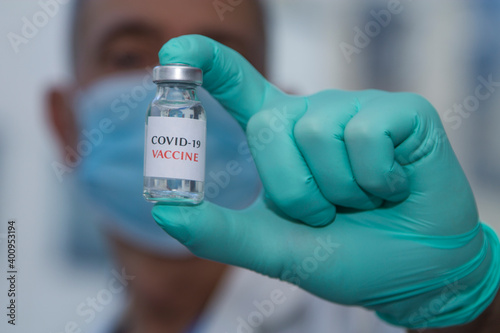 Healthcare cure concept with a hand in blue medical gloves holding Coronavirus, Covid 19 virus, vaccine vial