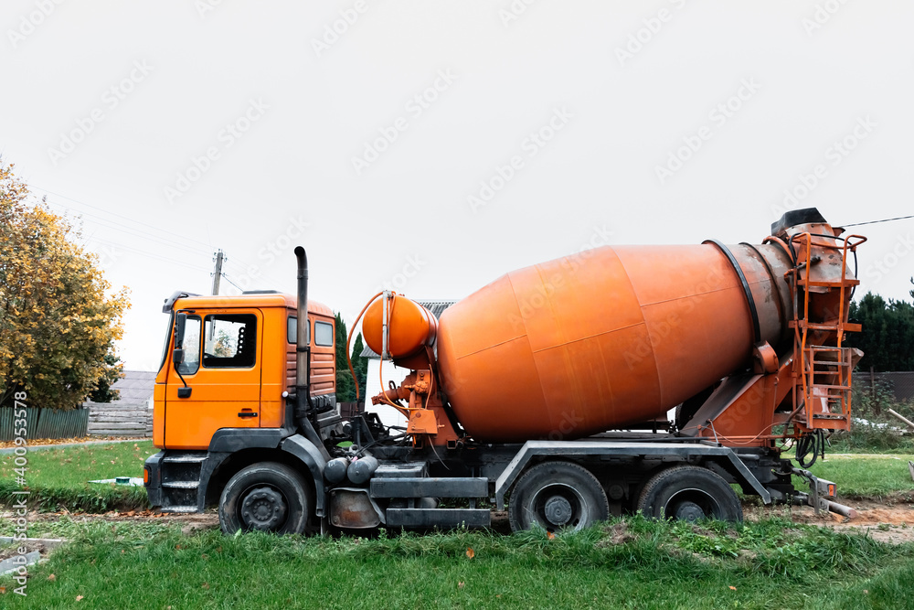 A large orange concrete mixer has arrived at the construction site. Special equipment for the delivery of building material - ready mixing cement. Large construction special transport with copy space A large orange concrete mixer has arrived at the construction site. Special equipment for the delivery of building material - ready mixing cement. Large construction special transport with copy space