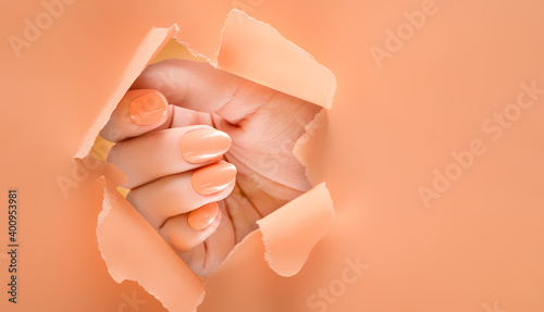 Female hand with orange nail design. Glitter Orange nail polish manicure. Woman hand on orange paper background