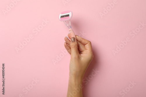 Female hand hold razor on pink background, space for text photo