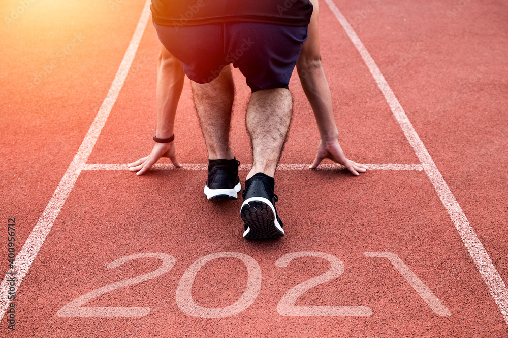 Fototapeta premium New year or start straight concept. Close Up on shoe of athlete runner running to success and new achievements on path with 2021 inscription. At sunset.