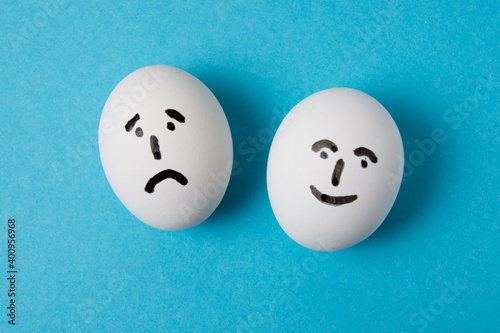 Eggs with faces and different emotions: sadness and joy. Isolate on a blue background.