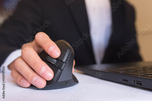 A person working at home in front of a computer holding a computer ergonomic mouse.