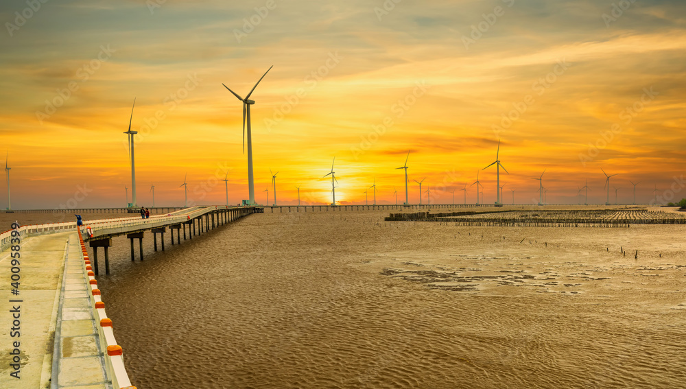 Clean energy, wind power plant in sunset sky with a pathway to the giant wind turbines at sea to provide electricity for human life.