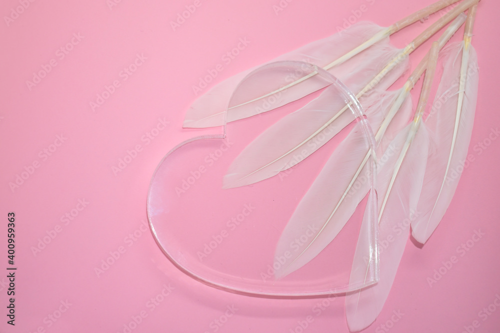 Transparent glass heart and white feathers on pale pink background. Place for your text. Valentine card, declaration of love, postcard, wedding invitation.