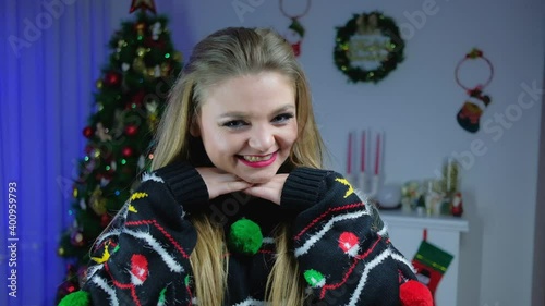 Cheerful beautiful shows emotions in slow motion 120 fps against the background of a Christmas tree in a New Year's sweater.