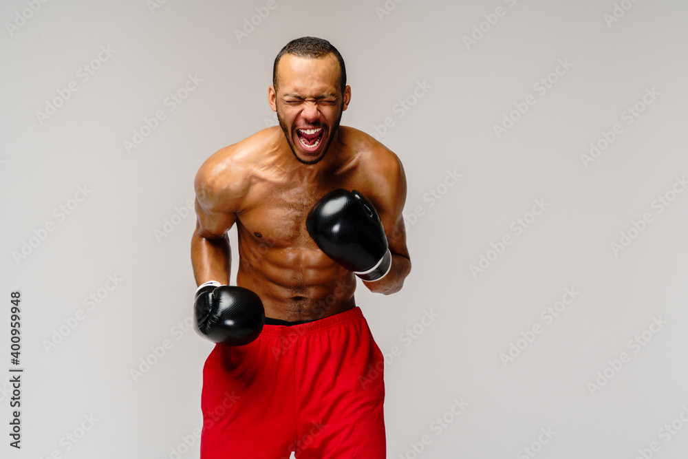 Confident young African boxer in boxing gloves standing over light grey background