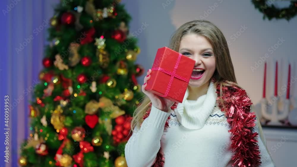 A Caucasian woman is turning in slow motion and showing the wrapping of a Christmas present in a cozy decorated room near a Christmas tree. Getting ready for the New Year holiday. A Caucasian woman is turning in slow motion and showing the wrapping of a Christmas present in a cozy decorated room near a Christmas tree. Getting ready for the New Year holiday.