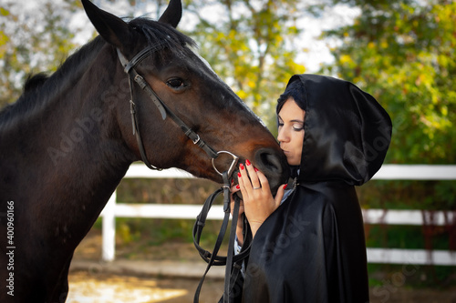 Girl in a black cloak hugs and kisses a horse