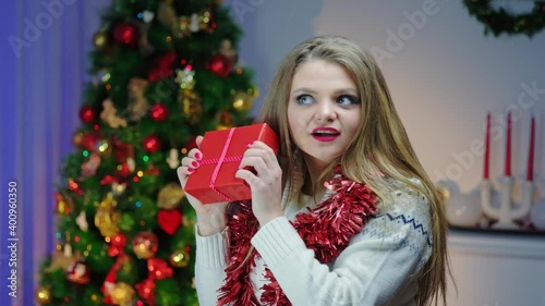 Blond woman in slow motion rejoicing at a Christmas present in a cozy decorated room near a Christmas tree. Getting ready for the New Year holiday.