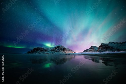 Aurora borealis on the Beach in Lofoten islands, Norway. Green northern lights above mountains. Night sky with polar lights. Night winter landscape.