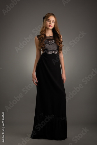 beautiful girl in a black dress posing in the studio on a gray background
