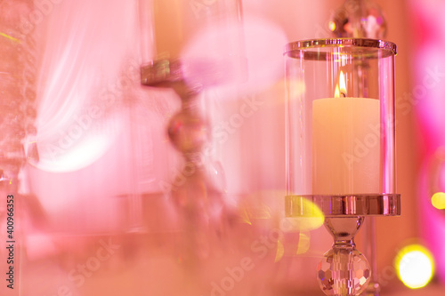 Fototapeta Naklejka Na Ścianę i Meble -  festive wedding table with burning candles and crystal in pink light. Crystal candle holder as a center piece at a wedding reception.