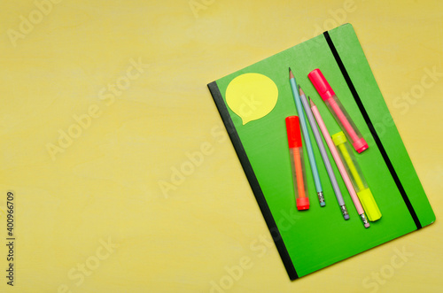 Top vuew of green notebook, colorful markers, note paper on the brigth yellow surface.Empty space