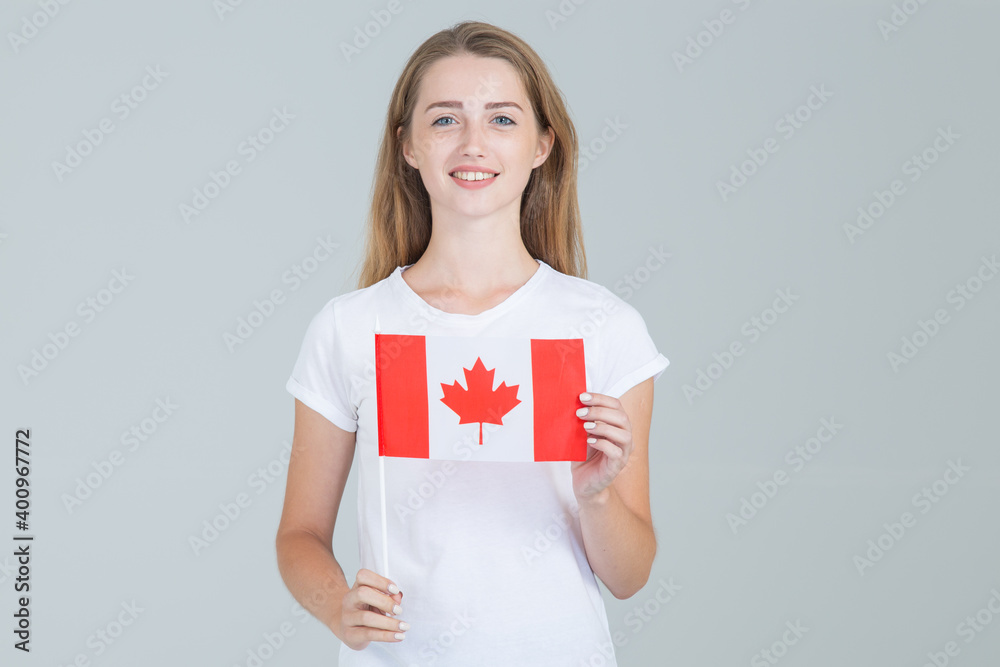 Young female student with the flag of Canada standing against gray background and looking at the camera. Young female student with the flag of Canada standing against gray background and looking at the camera.