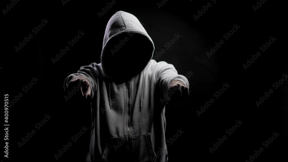 Mascots in the hands of a psychopath. Silhouette of a man with a darkened face in a hood on a black background. A portrait of a murderer, a hacker. Mascots in the hands of a psychopath. Silhouette of a man with a darkened face in a hood on a black background. A portrait of a murderer, a hacker.