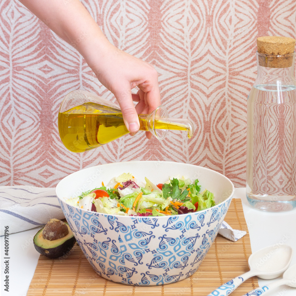 Woman's hand adding olive oil to salad