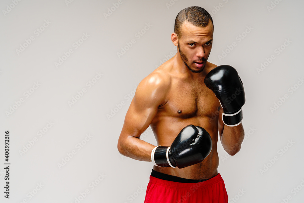 Confident young African boxer in boxing gloves standing over light grey background