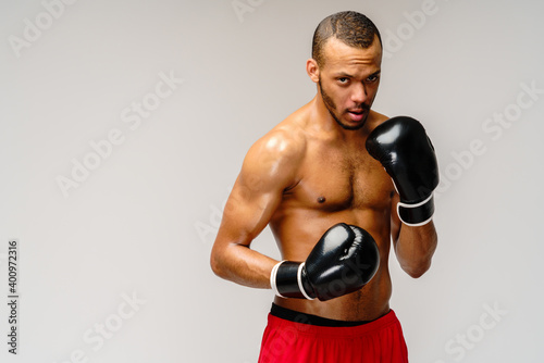 Confident young African boxer in boxing gloves standing over light grey background © Anatoly Repin
