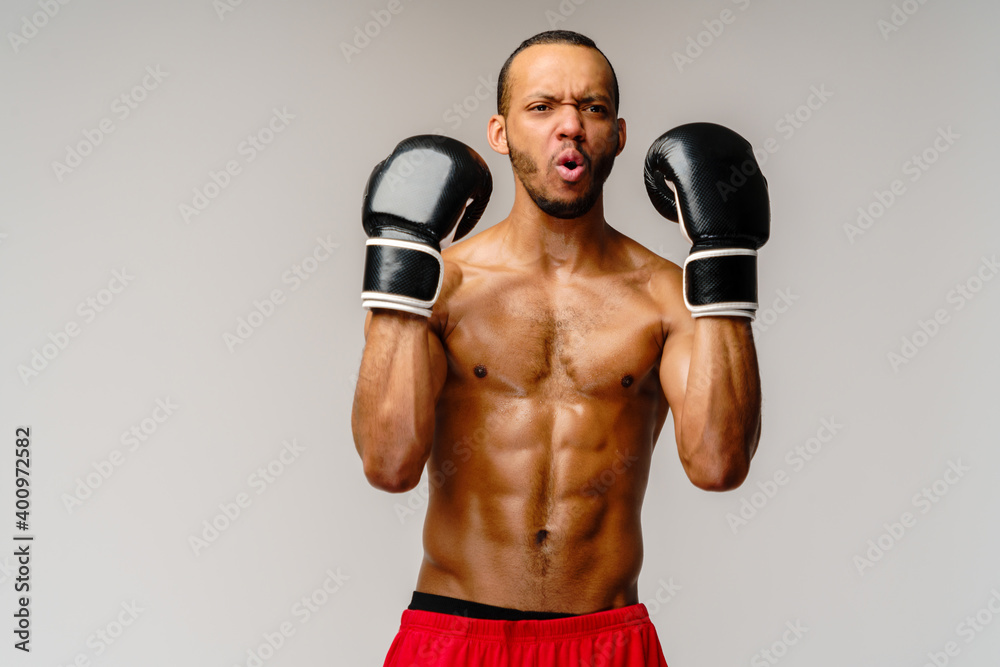 Confident young African boxer in boxing gloves standing over light grey background