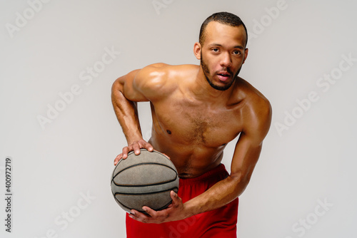 Muscular african american sportsman playing basketball shitless over light grey background photo