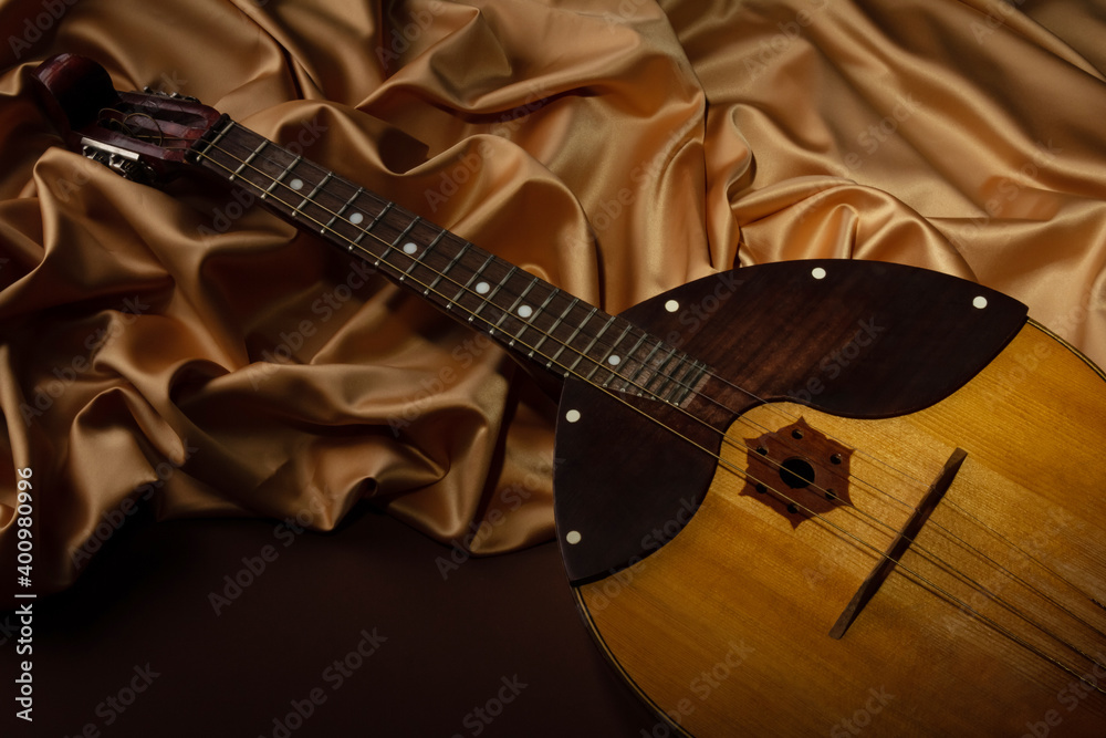 Fototapeta premium Domra musical instrument on background of folds of golden fabric