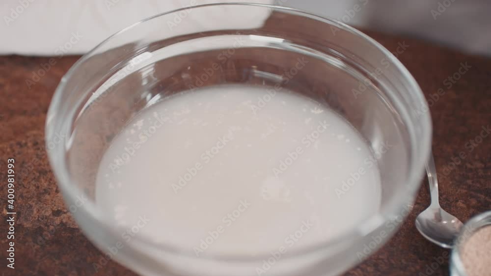 From-above shot of unrecognizable female hands adding sugar and flour in bowl with liquid mixture for homemade bread dough