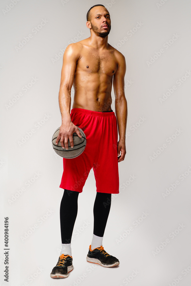 Fototapeta premium Muscular african american sportsman playing basketball shitless over light grey background