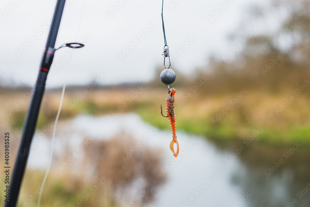 Lure made of silicone machine oil for fishing. Silicone bait for fishing hanging on a hook on the background of the river Lure made of silicone machine oil for fishing. Silicone bait for fishing hanging on a hook on the background of the river
