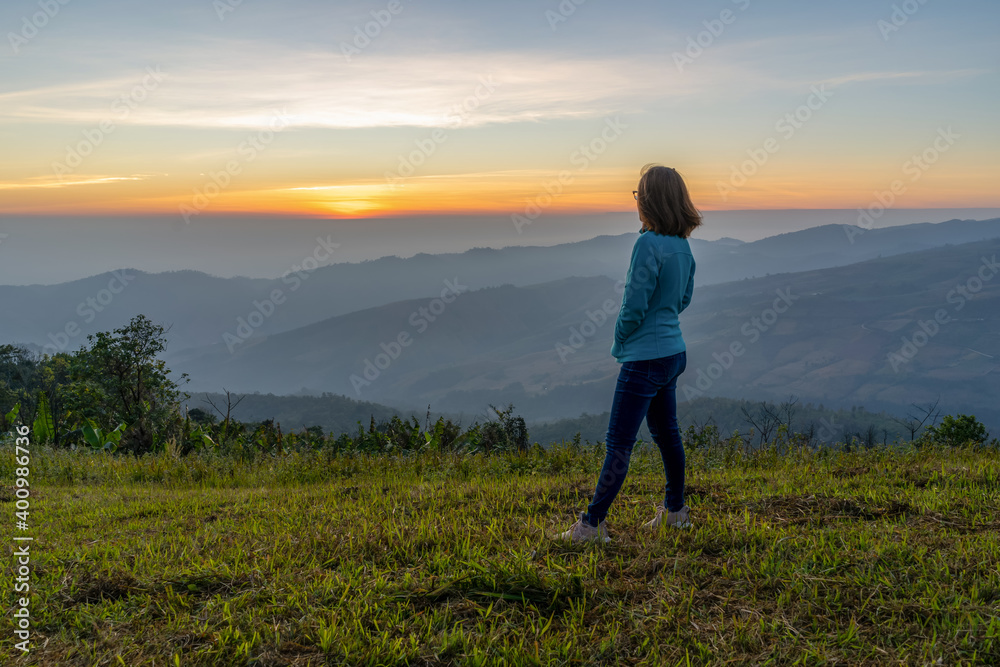 Young woman traveler looking at the sunrise over the mountain