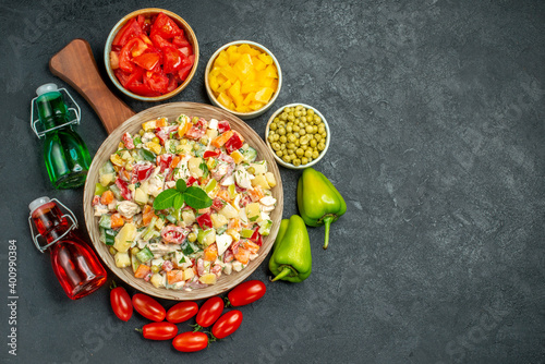 top view of bowl of vegetable salad on plate stand with vegetables and oil and vinegar bottles on side and place for your text on dark grey background
