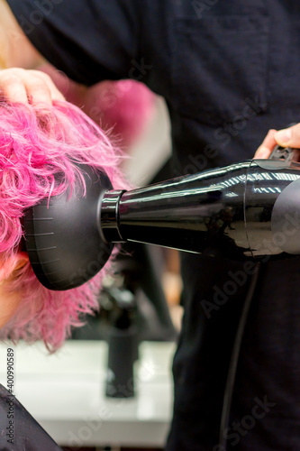 Close up of hairdresser drying short pink or red hair with a hairdryer in a beauty salon