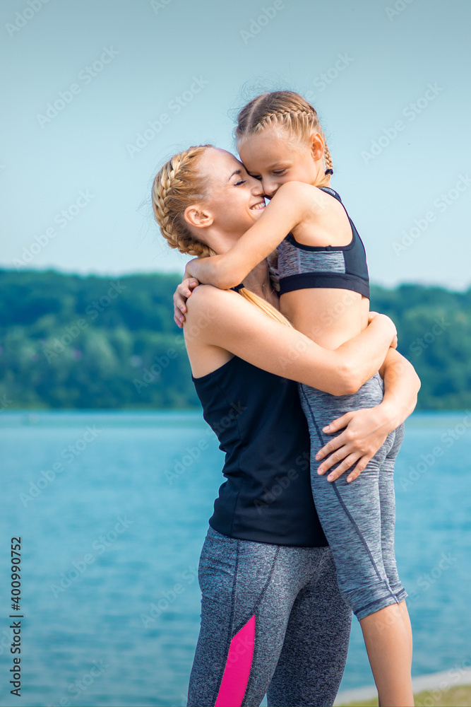 Mother embracing her daughter near the pond wearing sportswear outdoors