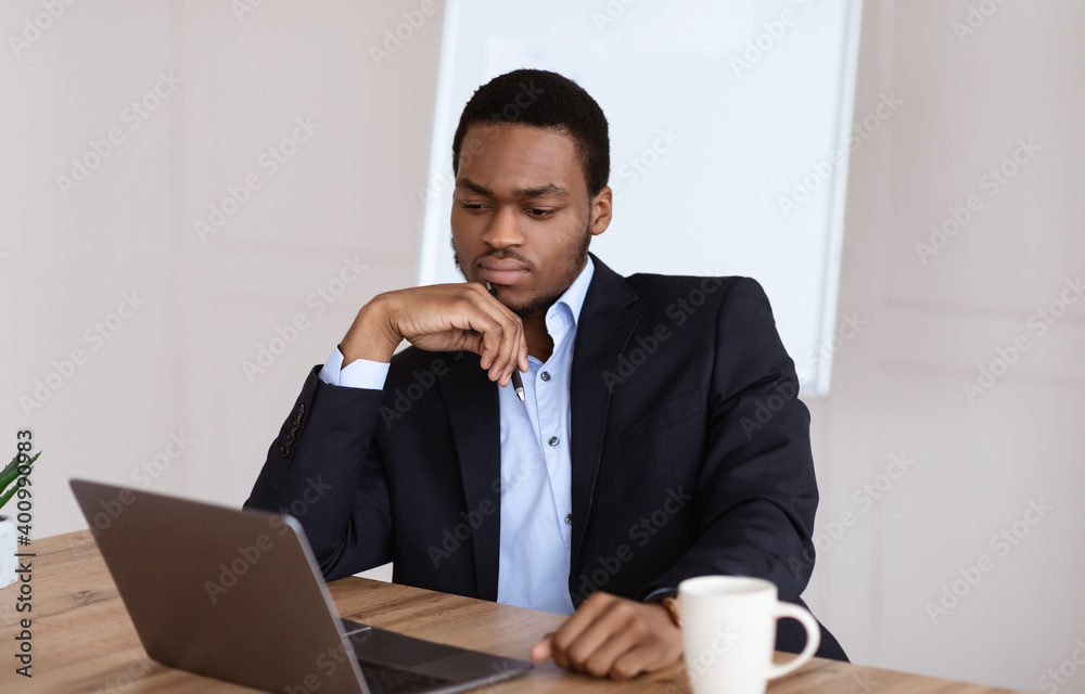Troubled black manager looking at laptop screen, office interior Troubled black manager looking at laptop screen, office interior