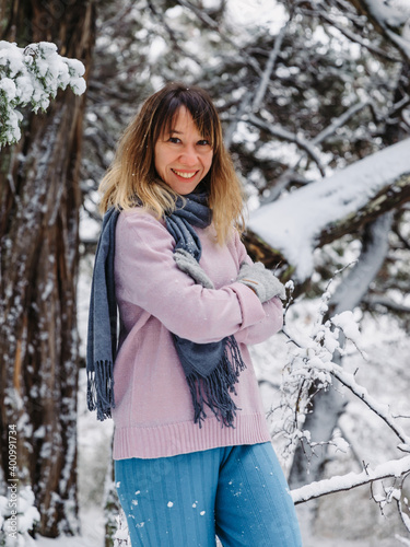 Happy young woman standing among snowy trees in winter forest and enjoying first snow