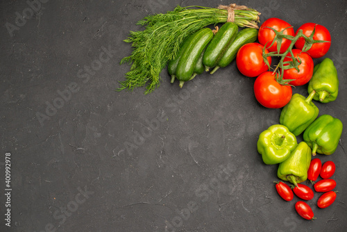 Horizontal view of fresh vegetables red tomatoes with stems green peppers and cucumbers a bunch of green necessary for cooking on dark background