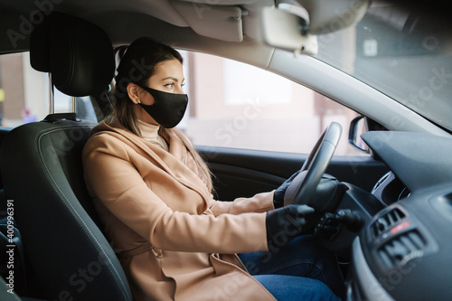 Beautiful young girl in a mask sitting in a car and put on protective gloves. Protective mask against covid-19, driver on a city street during a coronavirus outbreak