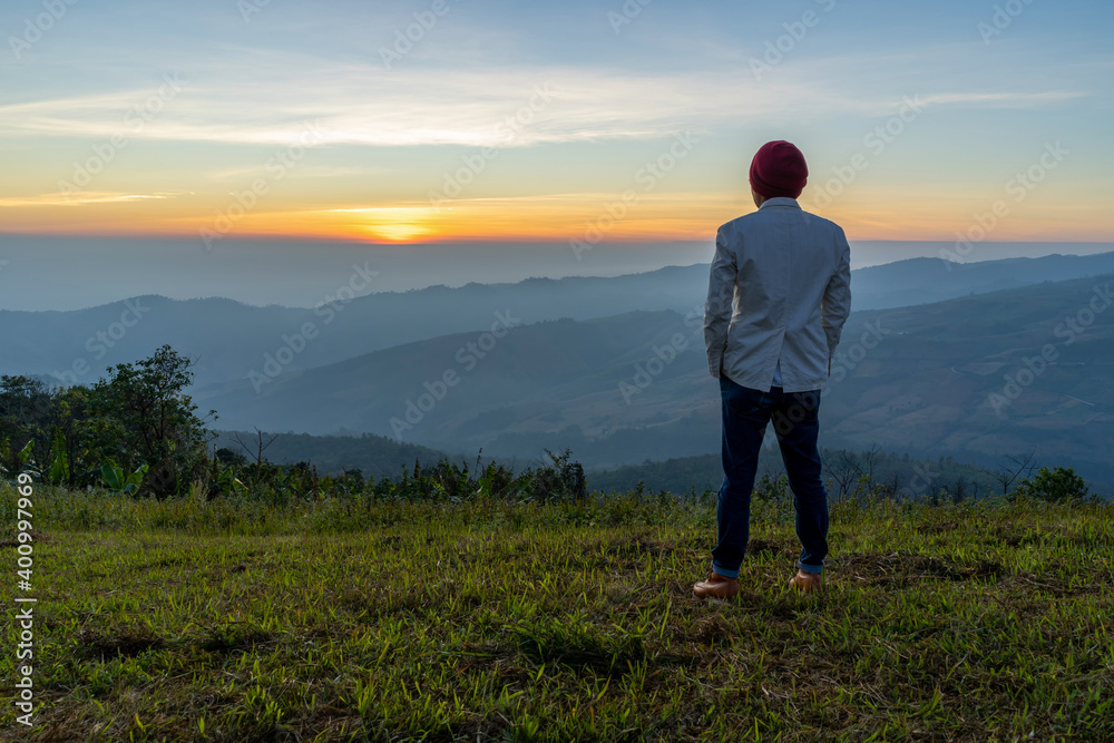 Young man traveler looking at the sunrise over the mountain