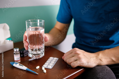 Hands man in holding pill and glass of water over table while sitting on couch and going to take medicine