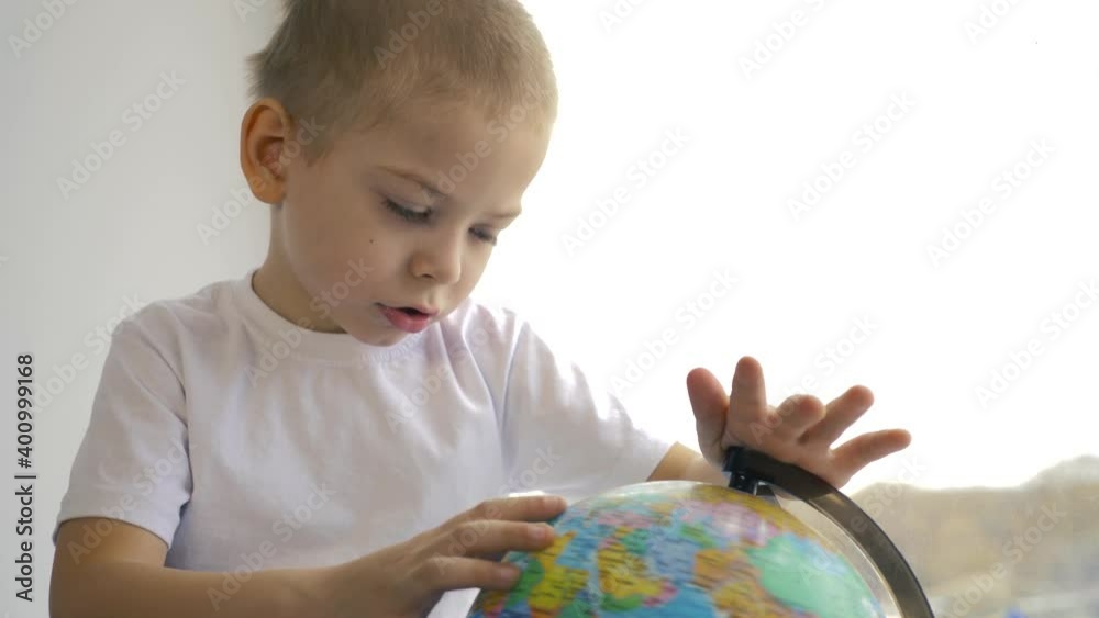 A curious boy sits at the window and studies the continents of the globe. Hobby of children at home, education of preschoolers. A curious boy sits at the window and studies the continents of the globe. Hobby of children at home, education of preschoolers.