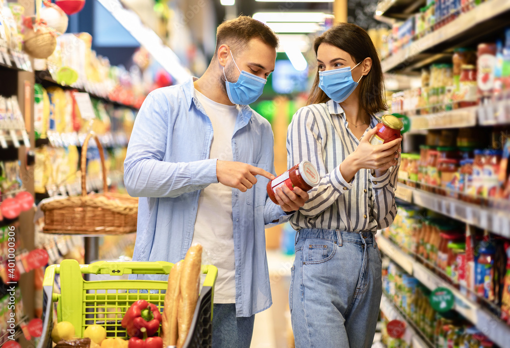 Young couple in disposable face masks shopping in supermarket