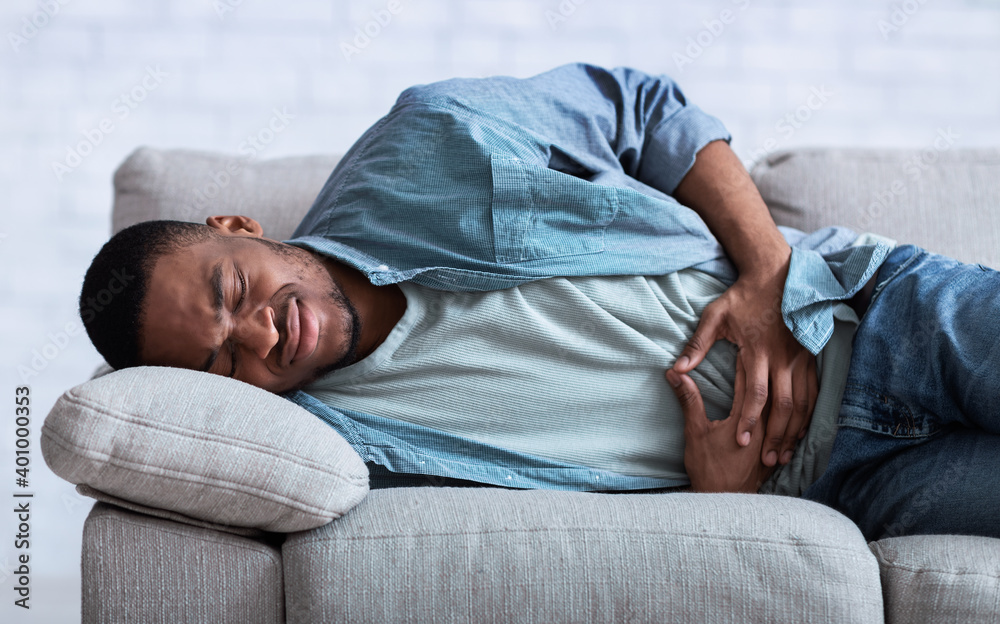 African Guy Suffering From Abdominal Pain Lying On Sofa Indoor African Guy Suffering From Abdominal Pain Lying On Sofa Indoor