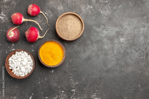 Horizontal view of different spices necessary for cooking dinner and red radishes on dark background