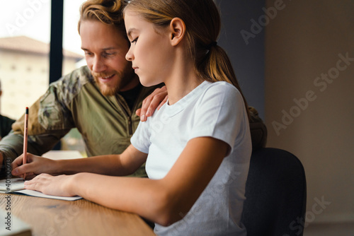 Masculine happy military man doing homework with her daughter at home