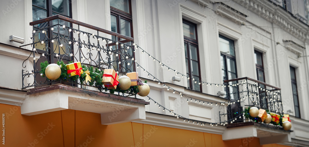 Balcony decorated for Christmas celebrations. Christmas decorations on facade of the building, festive decor and illumination, winter holidays. Gift box, garland lights hanging on balcony