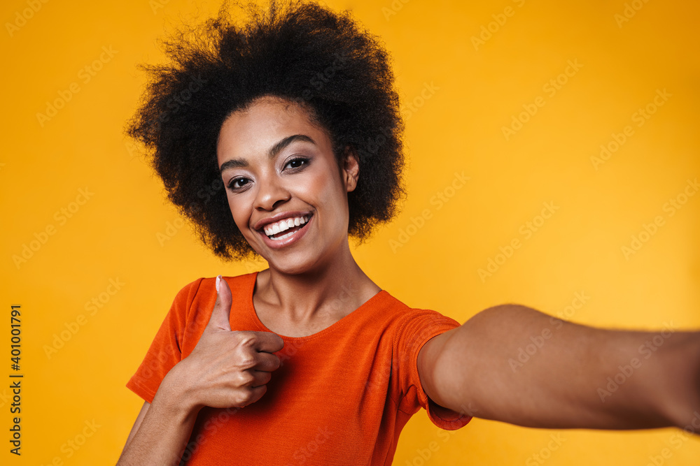 Joyful african american girl taking selfie while showing thumb up