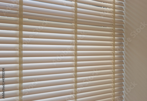 Wood blinds closeup in the interior. Automatic venetian blinds beige color on large windows. Coulisse wooden slats 50mm wide. Wood floor, beige walls.