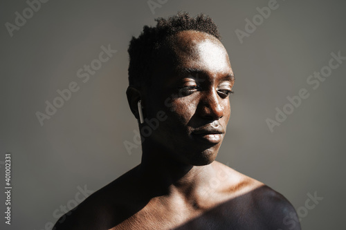 Close up portrait of a handsome fit muscular shirtless sportsman standing isolated over background, using wireless earphones